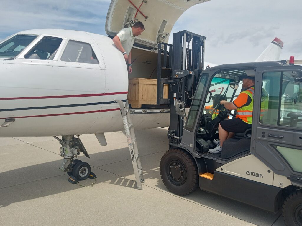 Forklift loading an AOG cargo crate through the main door of a Falcon jet on the ramp